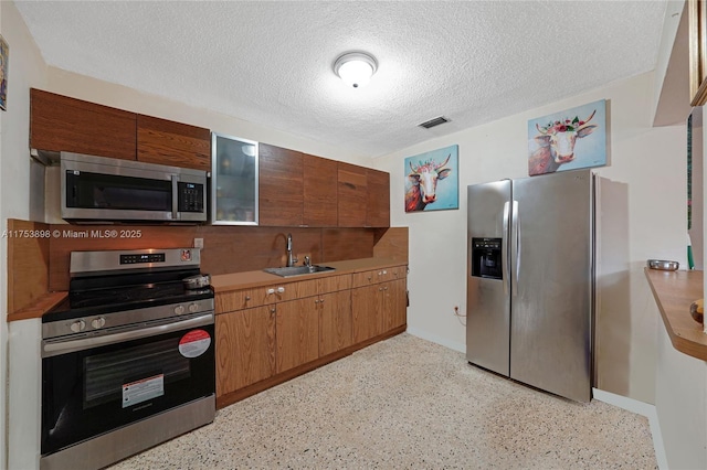 kitchen with a textured ceiling, a sink, visible vents, stainless steel appliances, and light speckled floor