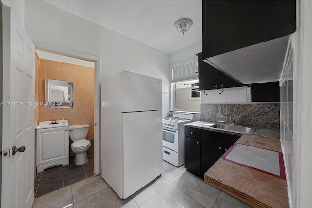 kitchen with a textured ceiling, light tile patterned floors, dark cabinets, white appliances, and a sink