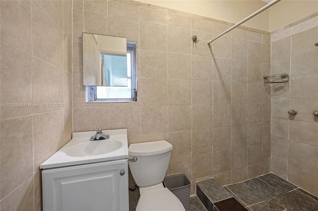 full bath featuring vanity, a tile shower, toilet, and tile walls