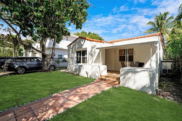 back of house with a lawn, fence, a tiled roof, and stucco siding