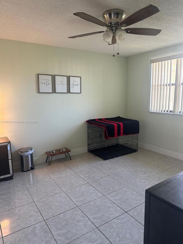 living area with ceiling fan, a textured ceiling, baseboards, and tile patterned floors