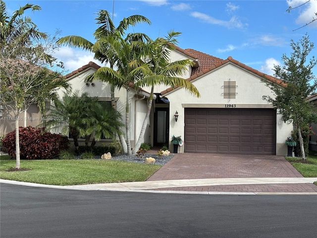 mediterranean / spanish-style home featuring an attached garage, a tile roof, decorative driveway, stucco siding, and a front yard