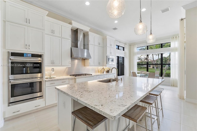 kitchen featuring light tile patterned floors, a center island with sink, wall chimney exhaust hood, appliances with stainless steel finishes, and a sink