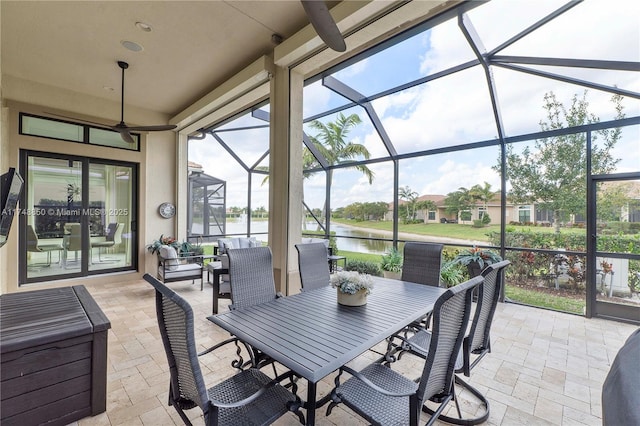 view of patio featuring outdoor dining space, glass enclosure, and a water view