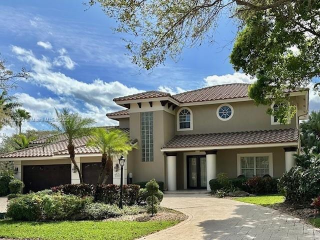 mediterranean / spanish-style house featuring french doors, a tile roof, stucco siding, an attached garage, and driveway