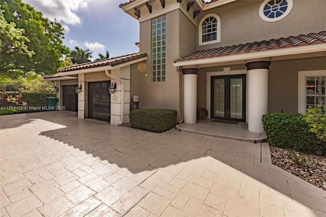 entrance to property featuring french doors, a tiled roof, an attached garage, and stucco siding