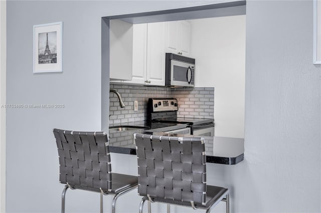 kitchen with decorative backsplash, dark countertops, appliances with stainless steel finishes, white cabinetry, and a sink