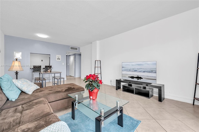 living room featuring light tile patterned floors, a textured ceiling, visible vents, and baseboards