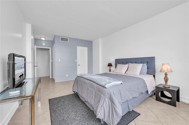 bedroom featuring light tile patterned floors, a closet, visible vents, a textured ceiling, and baseboards