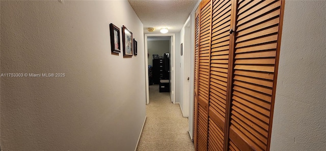 hallway with a textured ceiling, a textured wall, and light colored carpet