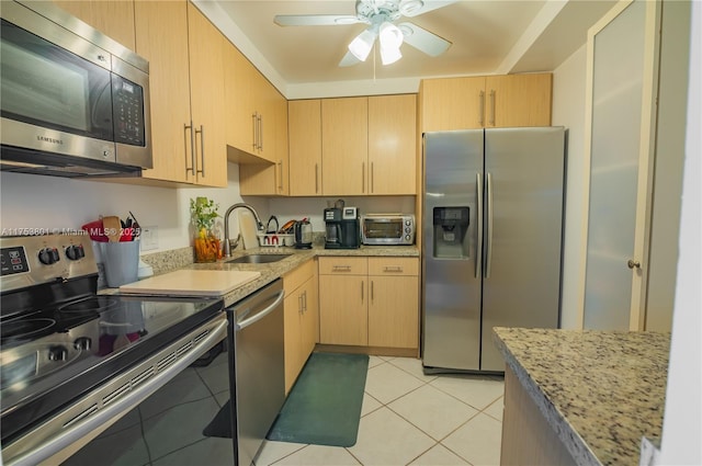 kitchen featuring stainless steel appliances, light brown cabinets, a sink, light tile patterned flooring, and light stone countertops