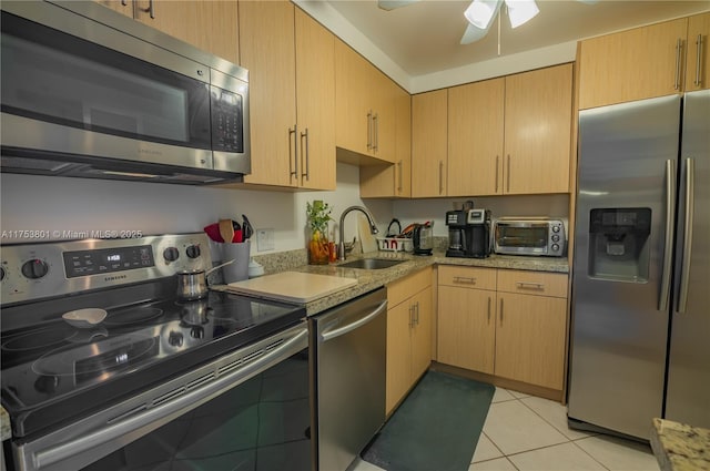 kitchen featuring light stone counters, light tile patterned flooring, a toaster, stainless steel appliances, and a sink