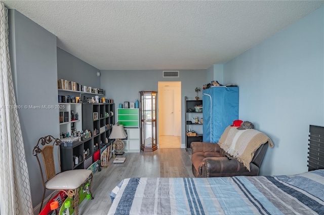 bedroom with a textured ceiling, wood finished floors, and visible vents