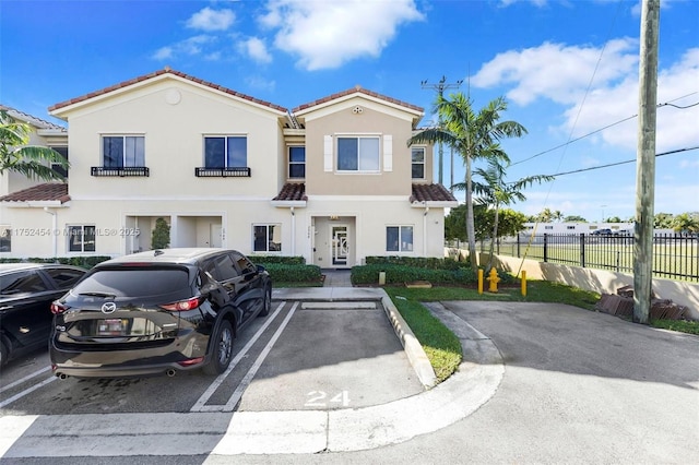 view of front of home featuring stucco siding, a tiled roof, fence, and uncovered parking