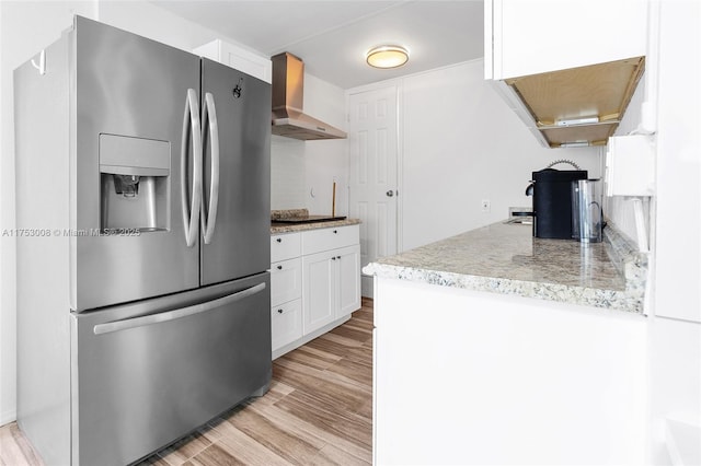 kitchen with black electric cooktop, white cabinetry, light wood-style floors, wall chimney exhaust hood, and stainless steel fridge