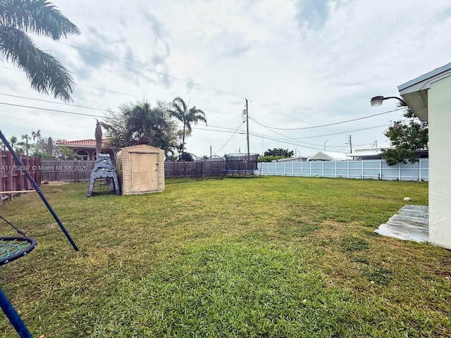 view of yard with a trampoline, a playground, a fenced backyard, and an outdoor structure