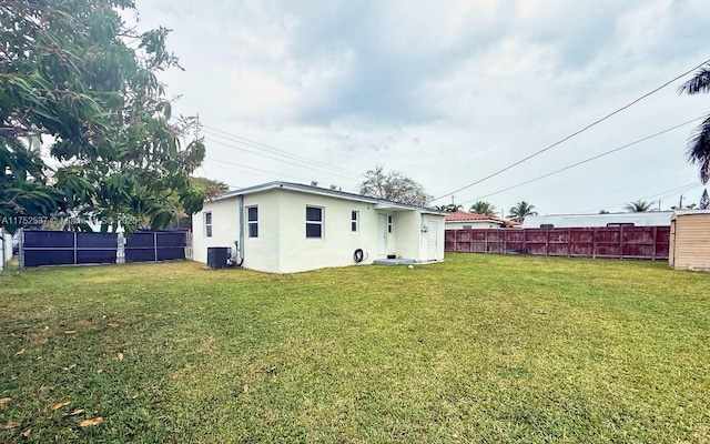 rear view of house featuring central AC, a yard, fence, and stucco siding