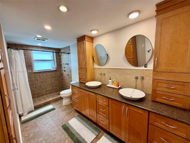 full bath with toilet, tiled shower, a sink, and visible vents