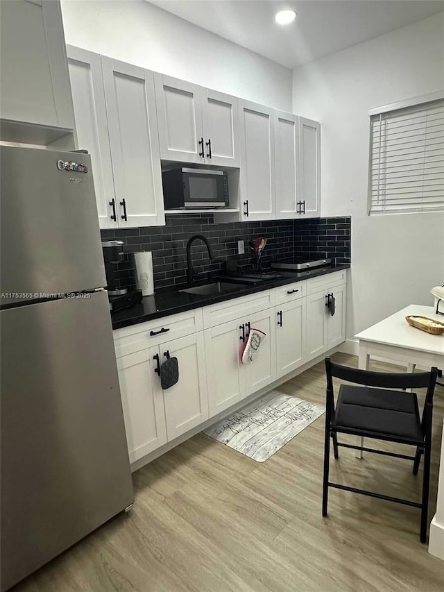 kitchen featuring light wood finished floors, tasteful backsplash, a sink, and freestanding refrigerator