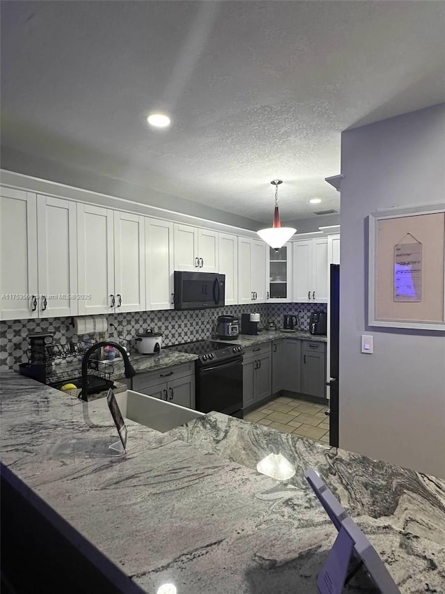 kitchen with light stone counters, backsplash, white cabinets, a sink, and black appliances