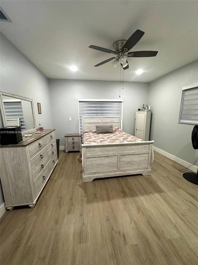 bedroom featuring a ceiling fan, visible vents, baseboards, and wood finished floors