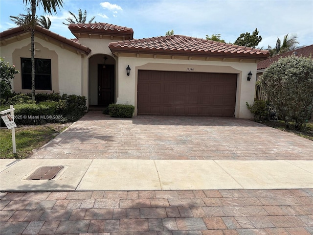 mediterranean / spanish home with stucco siding, a tiled roof, decorative driveway, and a garage