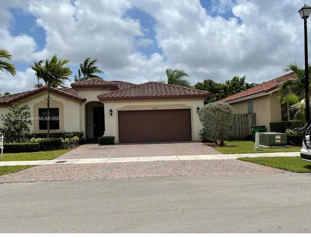 mediterranean / spanish house featuring a tiled roof, stucco siding, an attached garage, and decorative driveway