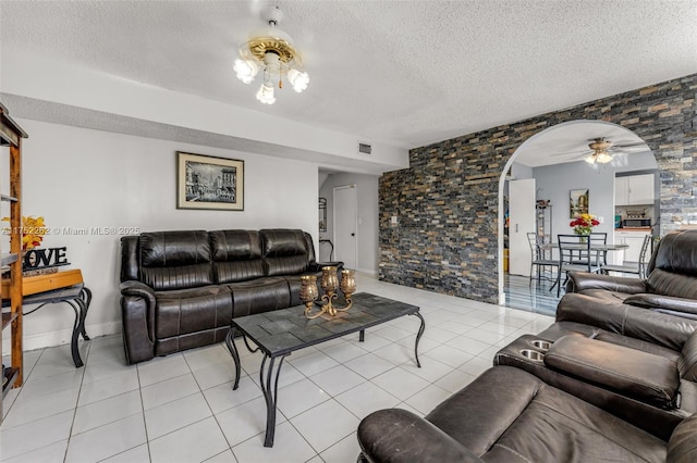 living area with visible vents, light tile patterned floors, arched walkways, a textured ceiling, and a ceiling fan