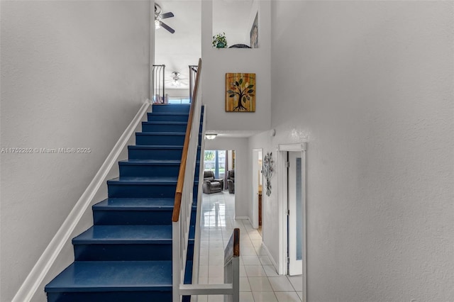 stairway featuring tile patterned flooring, a high ceiling, a ceiling fan, and baseboards