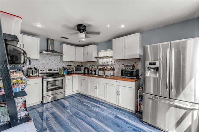 kitchen featuring tasteful backsplash, butcher block counters, white cabinets, stainless steel appliances, and wall chimney exhaust hood