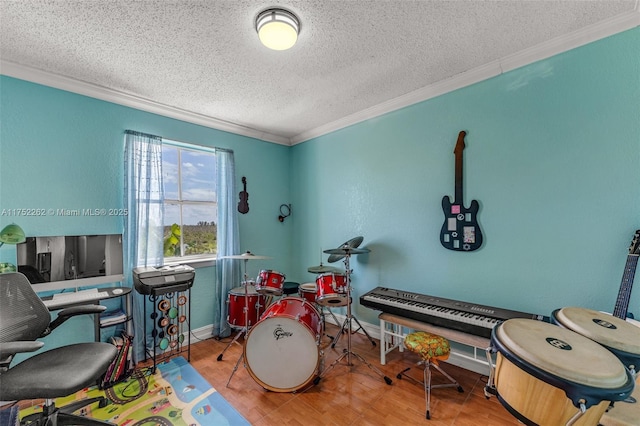 game room with a textured ceiling, crown molding, baseboards, and wood finished floors