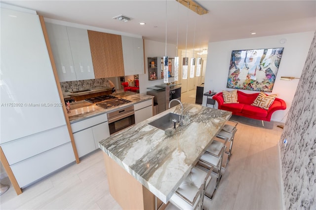 kitchen with an island with sink, modern cabinets, appliances with stainless steel finishes, a kitchen bar, and a sink