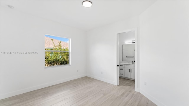 unfurnished bedroom featuring baseboards, a sink, connected bathroom, and light wood-style floors