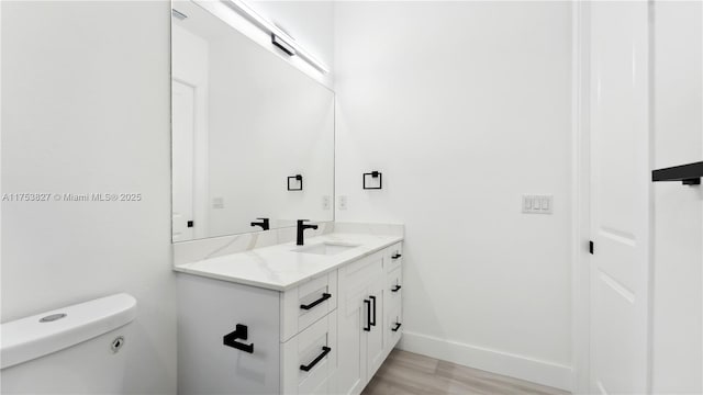 bathroom featuring toilet, vanity, baseboards, and wood finished floors