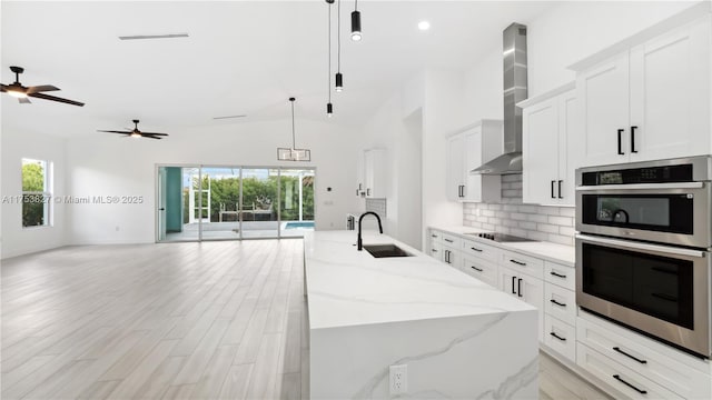 kitchen with black electric stovetop, a sink, open floor plan, wall chimney exhaust hood, and tasteful backsplash