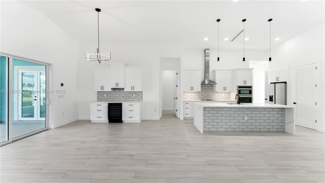 kitchen with beverage cooler, wall chimney exhaust hood, stainless steel appliances, light countertops, and a sink