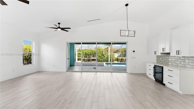 unfurnished living room with plenty of natural light, beverage cooler, ceiling fan, and light wood finished floors