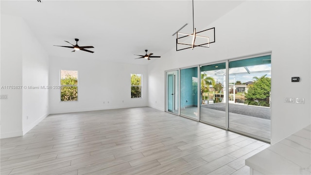 empty room with plenty of natural light, high vaulted ceiling, light wood-style flooring, and ceiling fan with notable chandelier