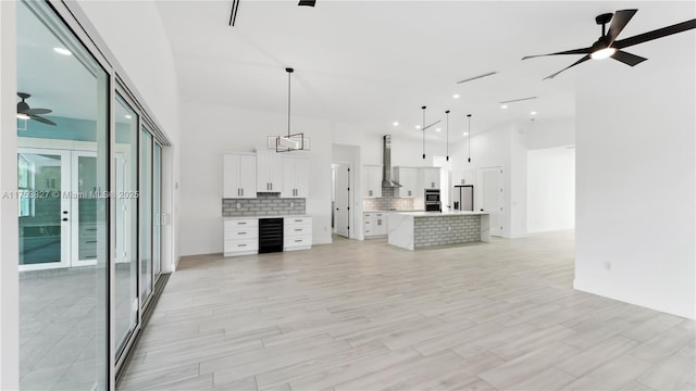 unfurnished living room with wine cooler, light wood-type flooring, a high ceiling, and a ceiling fan