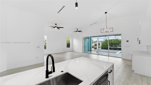 kitchen featuring white cabinets, hanging light fixtures, stainless steel dishwasher, light wood-type flooring, and light stone countertops