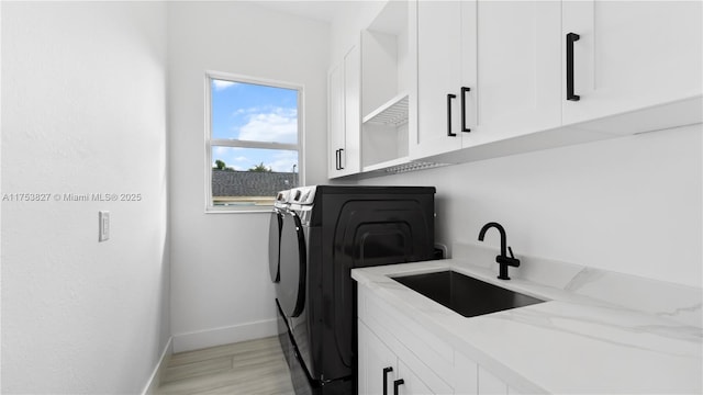 laundry area featuring cabinet space, baseboards, washing machine and clothes dryer, light wood-type flooring, and a sink