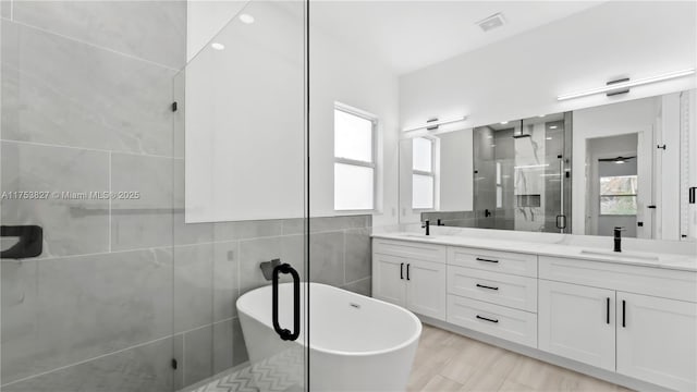 full bath featuring double vanity, plenty of natural light, a shower stall, and tile walls