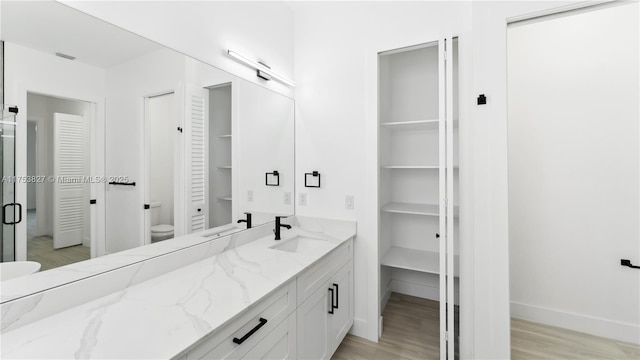 full bath with toilet, a stall shower, vanity, wood finished floors, and baseboards