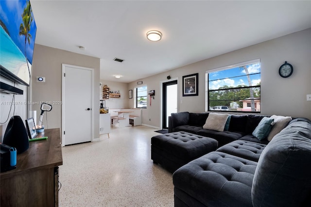 living area with baseboards, visible vents, and light speckled floor