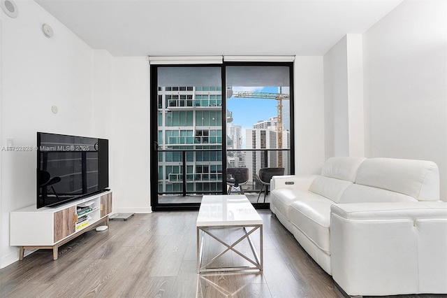 living room featuring a view of city, baseboards, a wall of windows, and wood finished floors