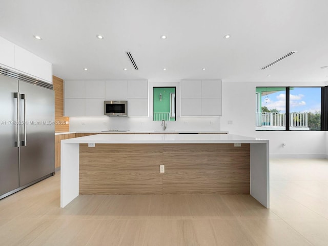 kitchen with appliances with stainless steel finishes, modern cabinets, white cabinetry, a spacious island, and light countertops