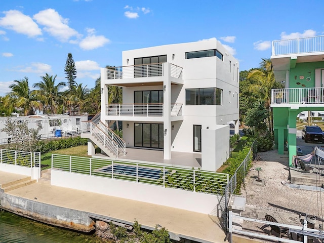 rear view of property with stucco siding, a fenced backyard, a balcony, a patio, and a water view