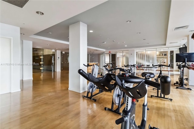 workout area with recessed lighting, visible vents, a tray ceiling, and wood finished floors