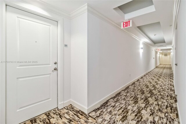 hall with a raised ceiling, baseboards, and ornamental molding