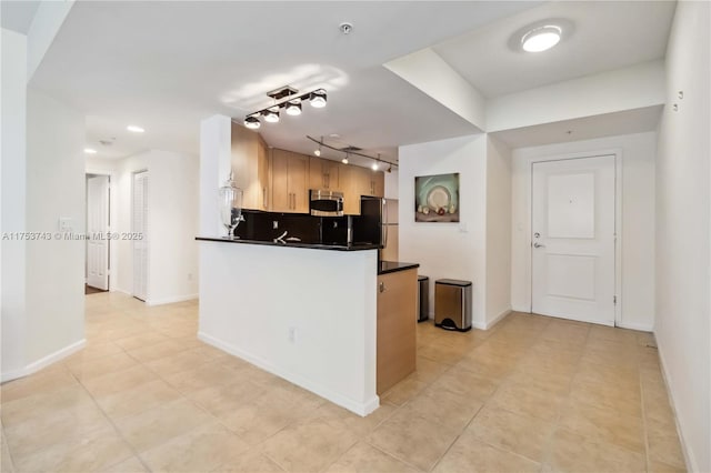 kitchen with dark countertops, stainless steel microwave, backsplash, freestanding refrigerator, and a peninsula